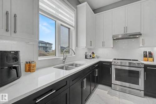 Contemporary kitchen featuring two-tone cabinetry, stainless steel appliances, a double basin sink, white subway tile backsplash, and quartz countertops - 3036 59 Avenue, Rural Leduc County, AB 