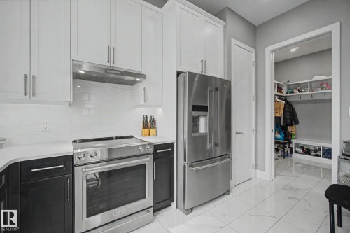 Modern kitchen featuring white upper cabinetry, dark lower cabinetry, and a stainless steel appliance suite including a French door refrigerator and electric range - 3036 59 Avenue, Rural Leduc County, AB 