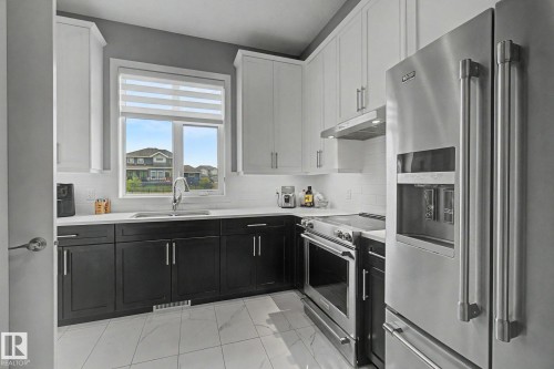 Modern kitchen featuring a two-tone cabinetry design with white upper cabinets and dark lower cabinets, white subway tile backsplash, and stainless steel appliances - 3036 59 Avenue, Rural Leduc County, AB 