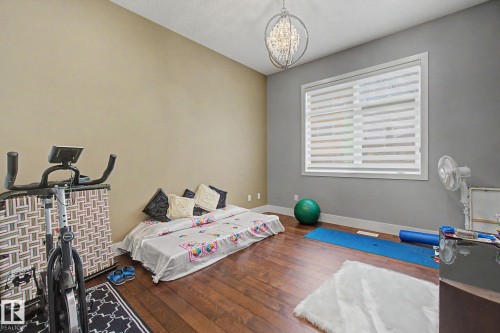 Interior room with wood-finish flooring, a large window with horizontal blinds, and a decorative orb chandelier - 3036 59 Avenue, Rural Leduc County, AB 