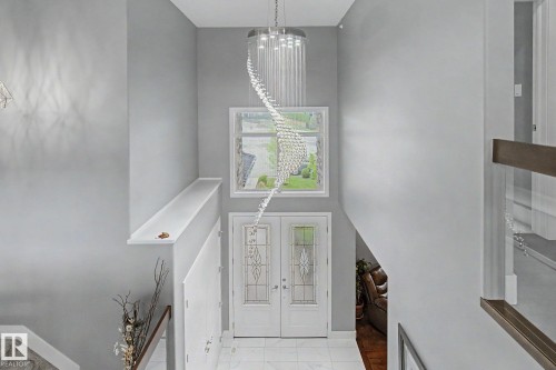 Two-story entryway featuring a crystal chandelier, twin entry doors with decorative glass inserts, and a transom window - 3036 59 Avenue, Rural Leduc County, AB 