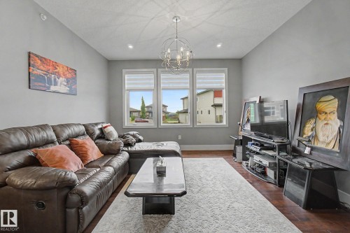 Living area featuring three large windows with blinds, wood-finish flooring, light gray walls, and recessed lighting, complemented by a contemporary spherical chandelier - 3036 59 Avenue, Rural Leduc County, AB 