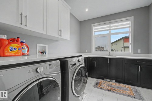 Laundry room featuring white shaker-style upper cabinetry, dark lower cabinetry, light countertops, and a single-basin sink - 3036 59 Avenue, Rural Leduc County, AB 