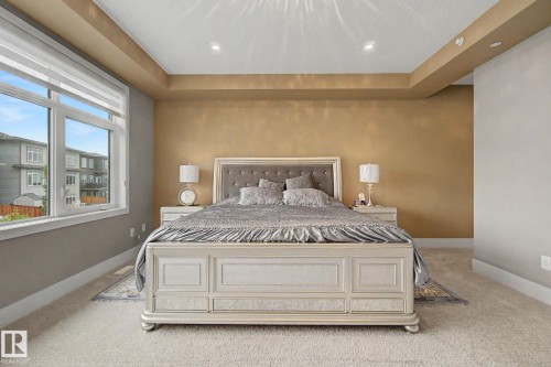 Spacious bedroom featuring a tray ceiling with recessed lighting, large window with roller shades, and plush carpet flooring - 3036 59 Avenue, Rural Leduc County, AB 