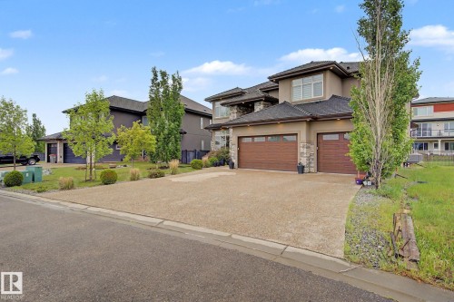Contemporary two-story residence featuring a stucco and stone facade, dual wood-finish garage doors, and an exposed aggregate driveway - 3036 59 Avenue, Rural Leduc County, AB 