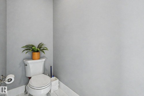 White toilet with a round bowl, chrome flush lever, and a wall-mounted toilet paper holder - 3036 59 Avenue, Rural Leduc County, AB 