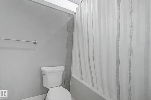 Three-piece bathroom featuring a white toilet, chrome towel bar, and tiled shower surround with a white bathtub - 3036 59 Avenue, Rural Leduc County, AB 