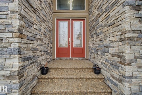 Stacked stone facade framing a double entry door with decorative glass inserts - 3036 59 Avenue, Rural Leduc County, AB 