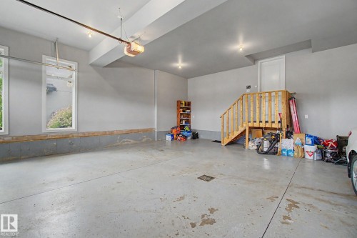 Spacious garage featuring a concrete floor, two large windows, a wooden staircase, and overhead lighting - 3036 59 Avenue, Rural Leduc County, AB 