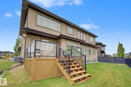 Rear exterior featuring a two-story stucco finish, a raised deck with glass panel railings, wood stairs, a fenced backyard, and multiple windows with blinds - 3036 59 Avenue, Rural Leduc County, AB 