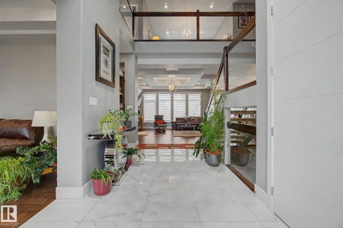 Foyer with polished marble-look tile flooring, a multi-level floor plan, wood-finish flooring, a contemporary staircase with glass railing, and coffered ceilings - 3036 59 Avenue, Rural Leduc County, AB 