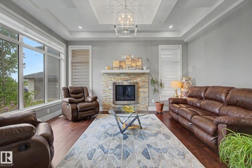 Spacious living area featuring a stone-clad fireplace, wood-finish flooring, and large picture windows - 3036 59 Avenue, Rural Leduc County, AB 