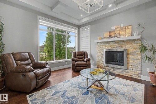 Living area featuring a floor-to-ceiling window, a coffered ceiling, wood-finish flooring, a contemporary fireplace with a stacked stone surround, and recessed lighting - 3036 59 Avenue, Rural Leduc County, AB 