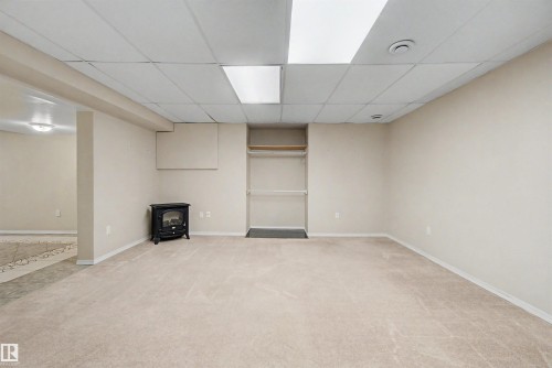 Spacious carpeted room featuring a drop ceiling with recessed lighting, an open closet with shelving, and a freestanding black stove - 2068 45 Street, Edmonton, AB - Indoor