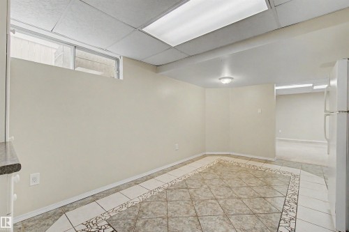 Spacious area featuring tile flooring with decorative mosaic border, recessed ceiling lighting, and a white refrigerator - 2068 45 Street, Edmonton, AB - Indoor Photo Showing Other Room