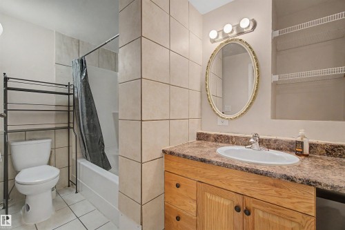 Full bathroom featuring a vanity with wood cabinetry, an oval mirror, and a tile tub surround - 2068 45 Street, Edmonton, AB - Indoor Photo Showing Bathroom