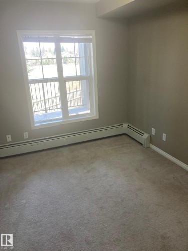 Carpeted room featuring a large window, baseboard heating, and light-toned walls - #206 616 Mcallister Lo Sw, Edmonton, AB - Indoor Photo Showing Other Room