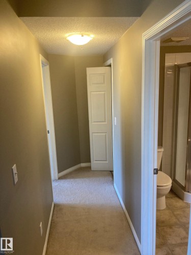 Hallway with neutral wall paint, light-colored carpet, and white baseboards - #206 616 Mcallister Lo Sw, Edmonton, AB - Indoor