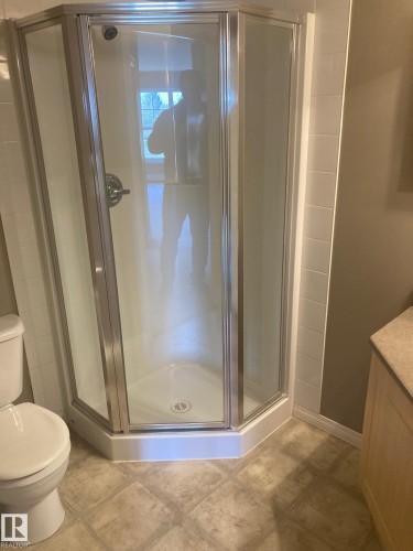 Corner shower enclosure with clear glass panels, chrome hardware, a white base, and a tiled surround - #206 616 Mcallister Lo Sw, Edmonton, AB - Indoor Photo Showing Bathroom