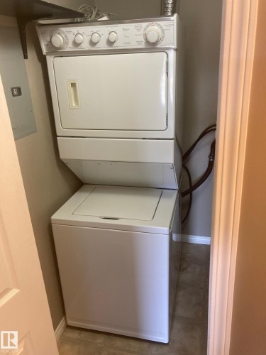 Dedicated laundry closet featuring a white stacked washer and dryer unit, utility connections, and a panel box - #206 616 Mcallister Lo Sw, Edmonton, AB - Indoor Photo Showing Laundry Room