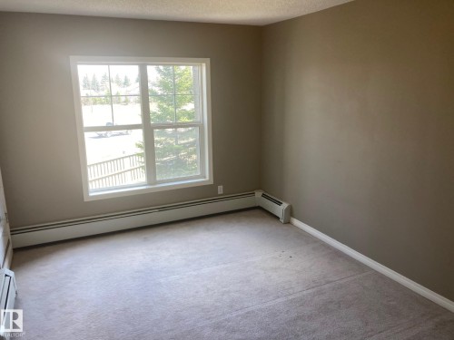 Carpeted room featuring neutral wall tones and a large window with white trim - #206 616 Mcallister Lo Sw, Edmonton, AB - Indoor Photo Showing Other Room