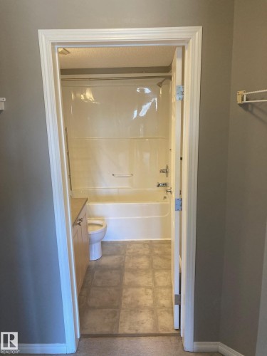 Bathroom featuring a white tub/shower combination unit with integrated soap dishes, a toilet, and a light wood-finish vanity with a countertop - #206 616 Mcallister Lo Sw, Edmonton, AB - Indoor Photo Showing Bathroom