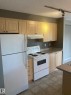 Kitchen featuring light wood-finish cabinetry, track lighting, a white refrigerator, a white electric range with an overhead exhaust, and durable flooring - #206 616 Mcallister Lo Sw, Edmonton, AB  - Indoor Photo Showing Kitchen 