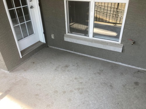 Outdoor patio area featuring textured stucco siding, a white gridded glass door, and a dual-pane window with a concrete sill - #206 616 Mcallister Lo Sw, Edmonton, AB - Outdoor