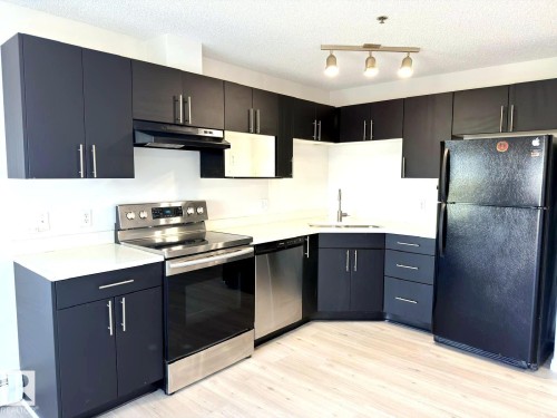Modern kitchen featuring dark cabinetry with brushed nickel hardware, white countertops, stainless steel appliances, and light wood-finish flooring - 312 2305 35A Avenue, Edmonton, AB 