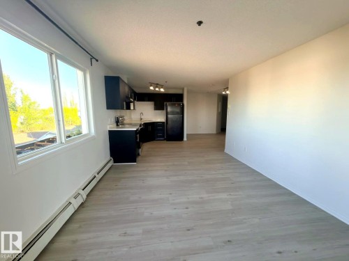 Open-concept living space featuring wood-finish flooring, white walls, and bright natural light from large windows - 312 2305 35A Avenue, Edmonton, AB 