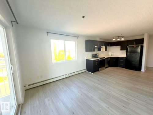 Open-concept kitchen and living area featuring wood-finish flooring, dark cabinetry, light countertops, and a full suite of kitchen appliances - 312 2305 35A Avenue, Edmonton, AB 