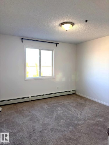 Carpeted room featuring a double-paned window, baseboard heating, a ceiling-mounted light fixture, and a window treatment rod - 312 2305 35A Avenue, Edmonton, AB 