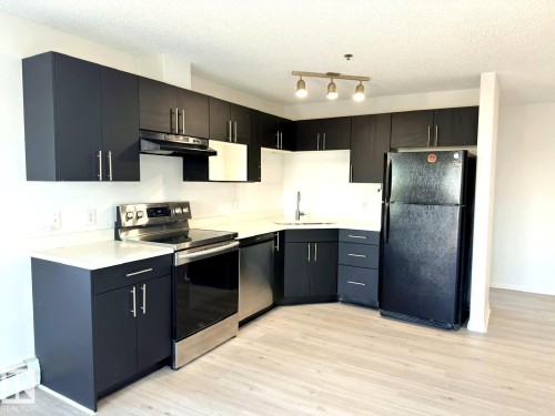 Kitchen featuring dark cabinetry, light countertops, and wood-finish flooring - 312 2305 35A Avenue, Edmonton, AB 
