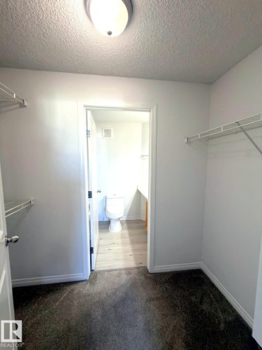 Carpeted closet space with wire shelving, offering direct access to a separate bathroom featuring wood-finish flooring and a toilet - 312 2305 35A Avenue, Edmonton, AB 