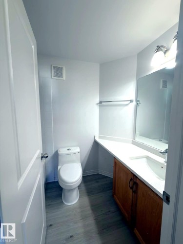 Bathroom featuring wood-finish flooring, a white vanity with an integrated sink, a wall-mounted mirror, and a white toilet - 312 2305 35A Avenue, Edmonton, AB 