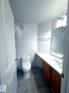 Bathroom featuring wood-finish flooring, a white vanity with an integrated sink, a wall-mounted mirror, and a white toilet - 