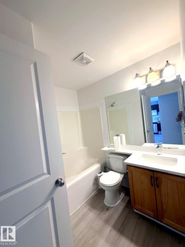 Bathroom featuring wood-finish flooring, a white porcelain bathtub, and a wood-tone vanity with a white countertop and integrated sink - 312 2305 35A Avenue, Edmonton, AB 