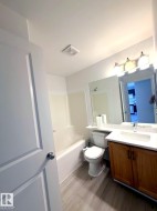 Bathroom featuring wood-finish flooring, a white porcelain bathtub, and a wood-tone vanity with a white countertop and integrated sink - 