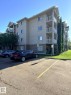 Multi-story building featuring stucco exterior, multiple balconies with white railings, a pitched roofline, and visible parking - 312 2305 35A Avenue, Edmonton, AB 