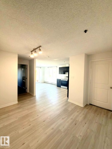 Open-concept living space featuring light wood-finish flooring, white walls, and a track lighting fixture - 312 2305 35A Avenue, Edmonton, AB 