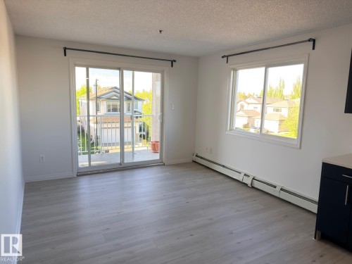 Spacious interior featuring wood-finish flooring, a large sliding glass door to the balcony, and an expansive window - 312 2305 35A Avenue, Edmonton, AB 