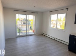 Spacious interior featuring wood-finish flooring, a large sliding glass door to the balcony, and an expansive window - 