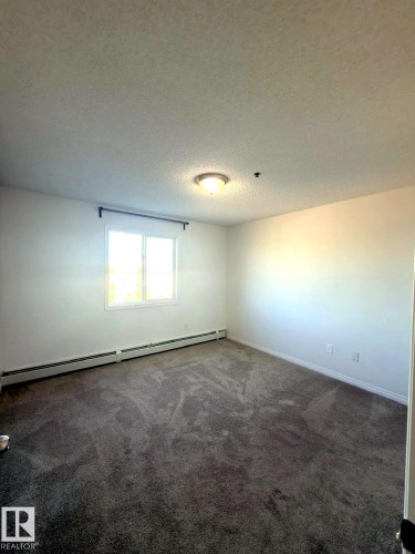 Spacious room featuring neutral carpeting, a large window, white walls, and baseboard heating - 312 2305 35A Avenue, Edmonton, AB 