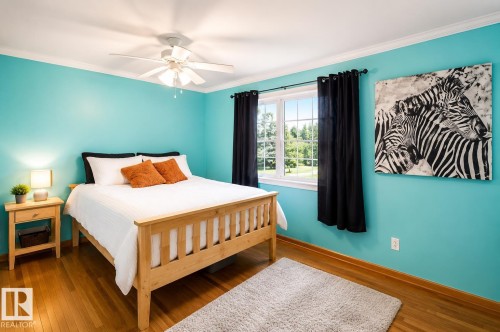 Bright room featuring wood-finish flooring, white crown molding, a ceiling fan with light fixture, and a window with a green outdoor landscape - 58124 Secondary 881, Rural St. Paul County, AB - Indoor Photo Showing Bedroom