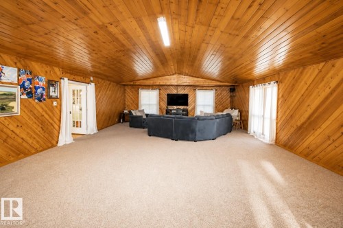 Spacious room featuring wood paneling on walls and ceiling, wall-to-wall carpeting, and multiple windows with white drapery - 58124 Secondary 881, Rural St. Paul County, AB - Indoor With Fireplace