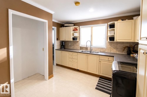 Kitchen area featuring cream-colored cabinetry, laminate countertops, a tile backsplash, and vinyl flooring - 58124 Secondary 881, Rural St. Paul County, AB - Indoor Photo Showing Kitchen With Double Sink