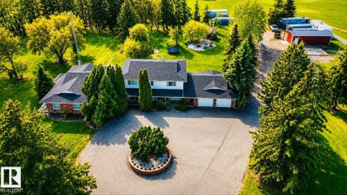 Expansive property featuring a large residence with a dark shingle roof, a circular driveway with a central landscaped island, mature evergreen trees, and a red barn structure - 58124 Secondary 881, Rural St. Paul County, AB - Outdoor