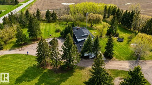 Expansive property featuring a dark-shingled roofline, surrounded by mature evergreen trees and vibrant green lawns - 58124 Secondary 881, Rural St. Paul County, AB - Outdoor With View