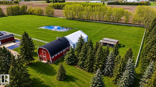Expansive green acreage featuring a red barn with a curved black roof, a large white hoop building, a second red outbuilding, mature evergreen trees, and perimeter fencing - 58124 Secondary 881, Rural St. Paul County, AB - Outdoor