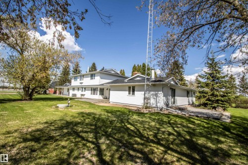Expansive lawn area featuring a white multi-level exterior, mature trees, and a stone patio - 58124 Secondary 881, Rural St. Paul County, AB - Outdoor